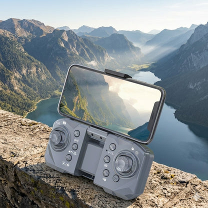 A professional close-up of the S14 Mini Drone grey remote controller resting on a rugged stone ledge. A smartphone is mounted on top, displaying a vibrant 1080p FPV live feed of a sunlit mountain range and a blue lake. The background features a matching, breathtaking real-world vista of misty alpine peaks and a valley, emphasizing the drone's portability for travel and outdoor exploration.